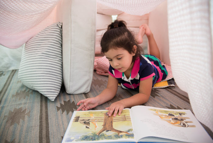young girl reads book inside blanket fort