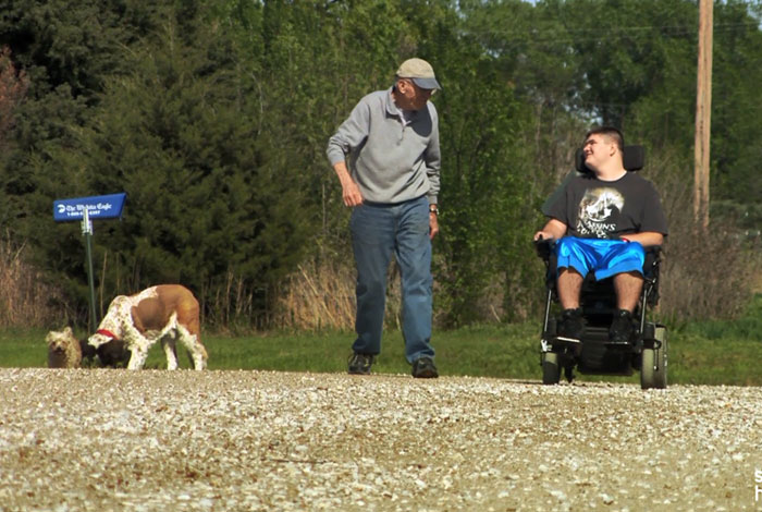 teenager in a wheelchair and grandfather walking a dog